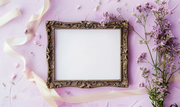 White blank card in a vintage bronze frame on a pastel lilac background, with a small bunch of wildflowers and a ribbon photo