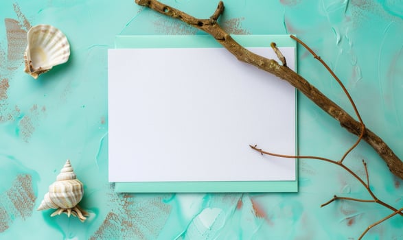 White blank card in a turquoise frame on a pastel turquoise background, with a seashell and a piece of driftwood photo