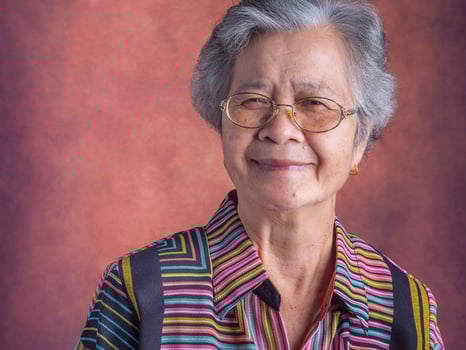 Portrait of a beautiful senior Asian woman wearing glasses with short white hair smiling and looking at the camera while standing with a vintage background. Concept of aged people and healthcare photo