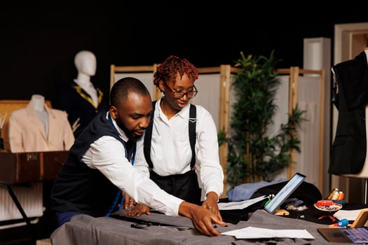 Refined masterful tailor team cutting fabric for bespoke modern fashion collection in dark studio. Elegant dressmakers manufacturing attire following dresses sketches photo