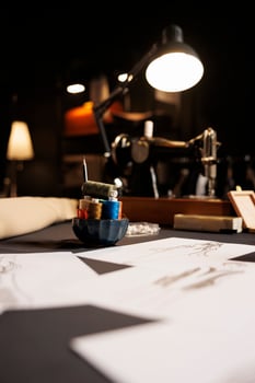 Table full of fashion designs on paper and sewing instruments in tailoring studio. Professional atelier shop workspace with sketch drawings, thread spools, sewing machine photo