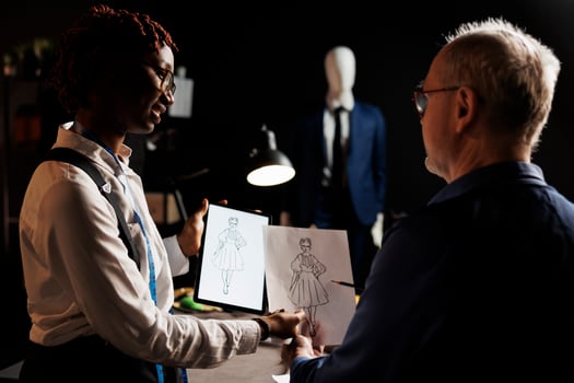 African american tailor apprentice and elderly master dressmaker comparing sketch drawing on tablet and paper, trying to design the perfect dress. Couturiers working on client comission photo