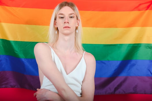 Young gay man 20s with make up wrapped in rainbow striped flag isolated on background, studio portrait. People lifestyle fashion lgbtq concept. photo
