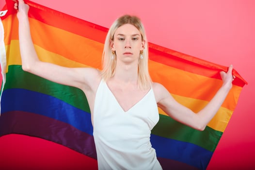 Young gay man 20s with make up wrapped in rainbow striped flag isolated on background, studio portrait. People lifestyle fashion lgbtq concept. photo