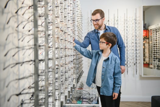 Dad and son choose new stylish glasses in an optical store. Vision care concept photo
