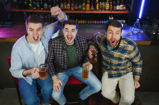 Soccer fans cheering for favourite team while enjoying drinks. Group of supporters celebrating victory while watching football match on tv in a club. Happy friends shouting while cheering for a goal. photo