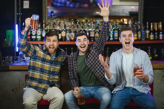 Soccer fans at the bar. Happy football fans cheering at bar and drinking beer while bartender serving beer at the background photo