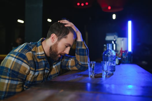 Sad young man sitting at bar counter in pub. Upset man drinks alcohol because of problems at work. photo