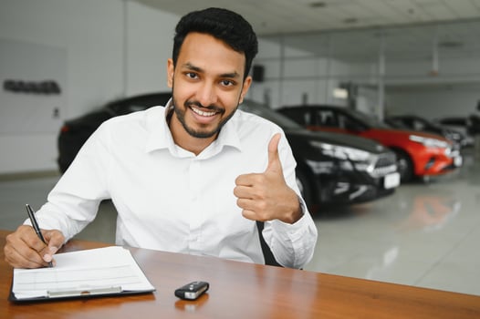 young indian man signing documents at car dealership photo