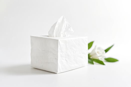 White Tissue Box with White Flower and Green Leaves on a White Background photo