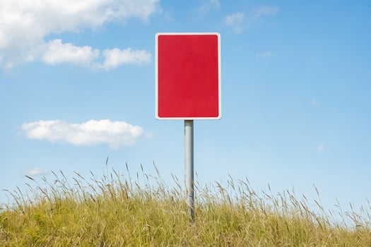 Red Blank Sign in Grass Field Against Blue Sky photo