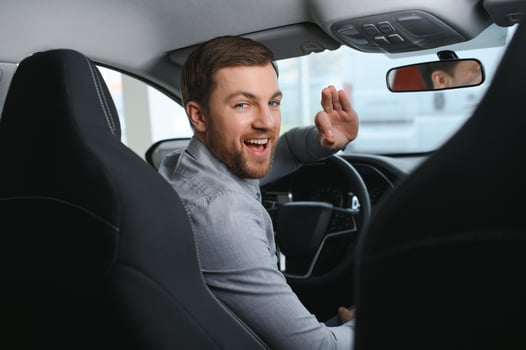 Taxi driver smiling while turning over to the backseat looking talking with clients. Successful businessman husband looking at the backseat at dealer shop before buying a car photo