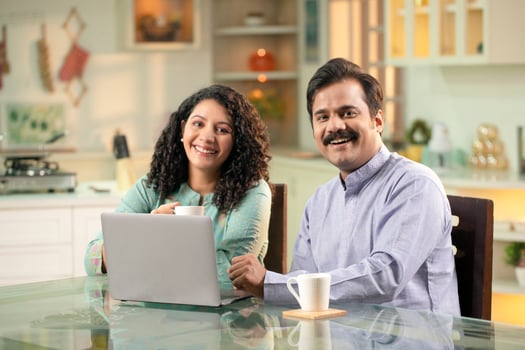Young Couple Sitting In Front Of Laptop Smiling While Looking At Camera photo