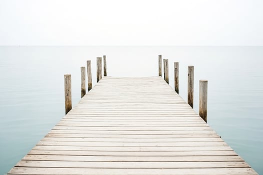 Wooden pier leading out to calm sea with white sky photo