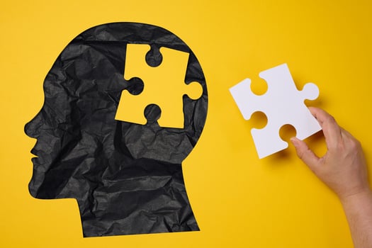 Silhouette of a human head holding a puzzle piece on a yellow background, representing mental health photo