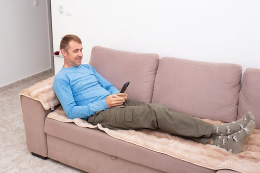 A cheerful man is texting his friends and agreeing on a meeting place while sitting on the sofa in his living room photo