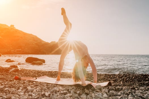 Woman sea yoga. Happy woman in white swimsuit and boho style braclets practicing outdoors on yoga mat by sea on sunset. Women yoga fitness routine. Healthy lifestyle, harmony and meditation photo