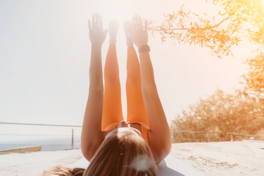 Fitness woman sea. Happy middle aged woman in orange sportswear exercises morning outdoors on yoga mat with laptop in park over ocean beach. Female fitness pilates yoga routine. Healthy lifestyle. photo
