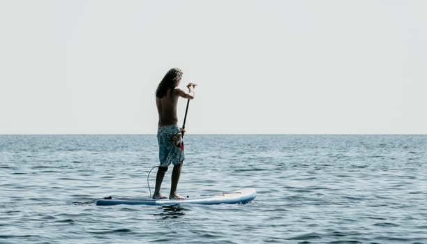 Man Sup Sea. Strong athletic man learns to paddle sup standing on board in open sea ocean on sunny day. Summer holiday vacation and travel concept. Aerial view. Slow motion photo