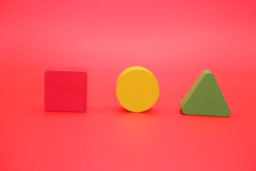 colorful wooden toys isolated red background. wooden toys shaped like triangles, squares and circles. photo