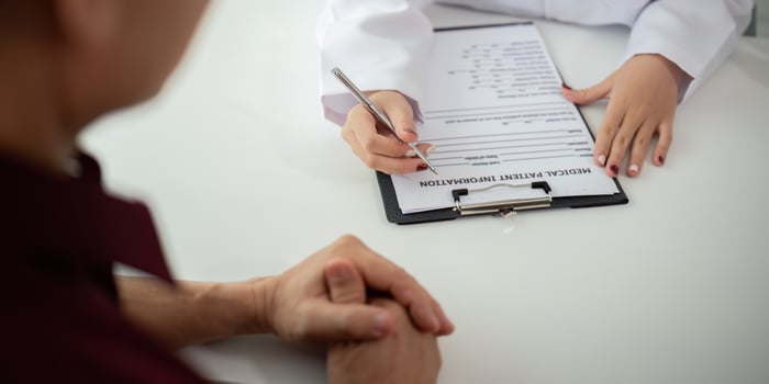 Doctor consulting male elderly patient filling medical form. Professional physician writing information in clipboard checking examining elderly man during appointment visit in clinic photo