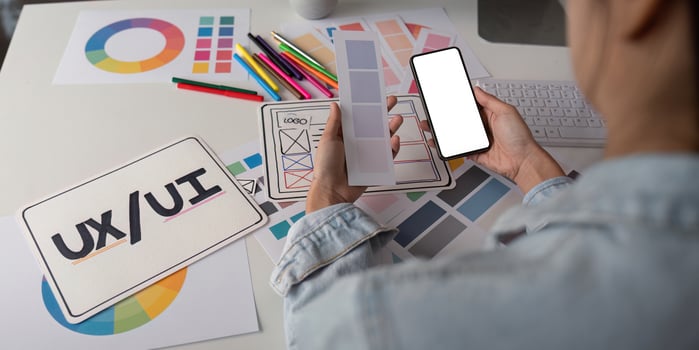 Woman hands holding a smartphone white screen mockup over modern graphic designer office desk photo