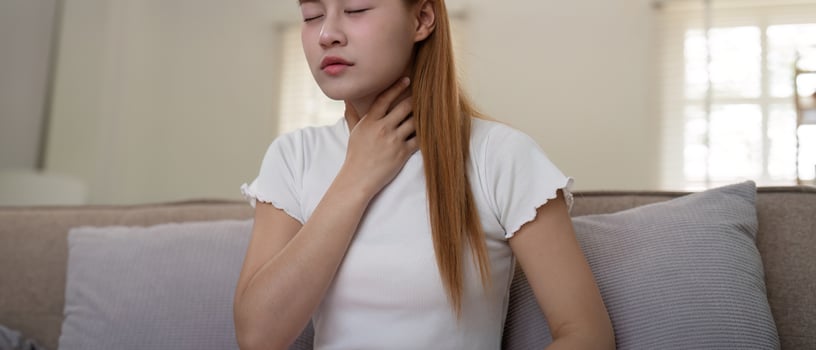 Young woman experiencing throat pain while sitting on a sofa at home photo