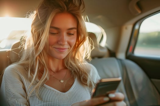 Smiling woman using smartphone in back seat of car during daytime drive photo