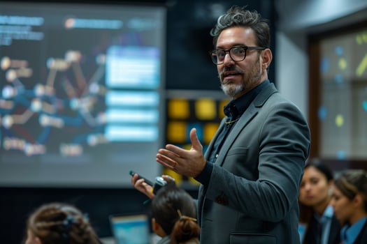 A businessman is presenting information to an audience, gesturing towards a large screen displaying data visualization. The man is wearing a suit and glasses, and the audience is attentive photo