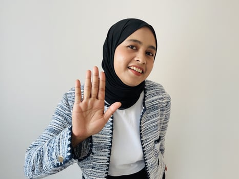 Portrait shot of young Asian Muslim young happy charming female model in casual clothing and hijab smiling hold hand up greeting say hello hi gesture photo