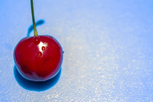 A cherry is sitting on a blue surface. The cherry is red and shiny photo