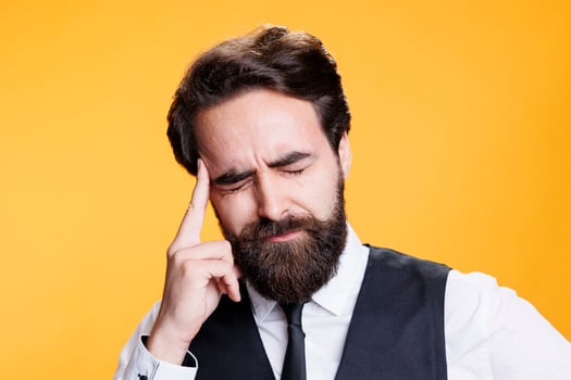 Skilled butler deals with migraine against yellow background on camera, feeling ill from pain and rubbing temples. Young adult being overworked with bad headache, burnout concept. photo