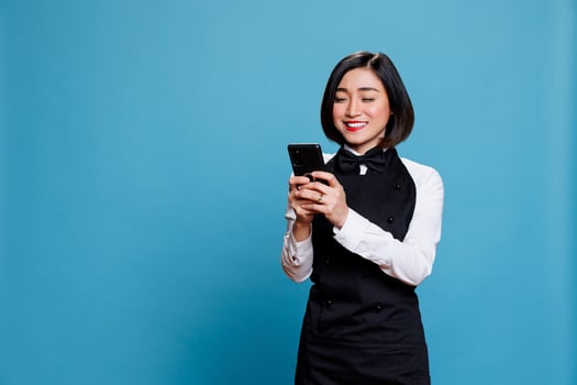 Hotel receptionist holding smartphone and checking message from satisfied customer. Asian waitress with excited face expression reading service positive reviews on mobile phone photo