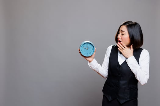 Asian waitress overslept and running late for work at cafe while yawning and looking at alarm clock. Restaurant sleepy woman employee wearing professional uniform showing time photo