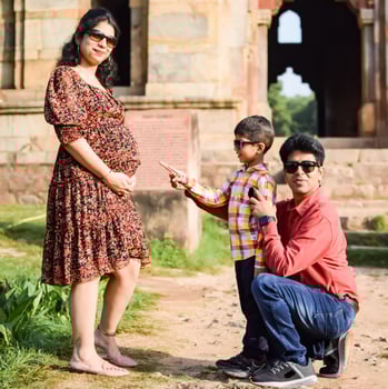Indian couple posing for maternity baby shoot with their 5 year old kid. The couple is posing in a lawn with green grass and the woman is flaunting her baby bump in Lodhi Garden in New Delhi, India photo