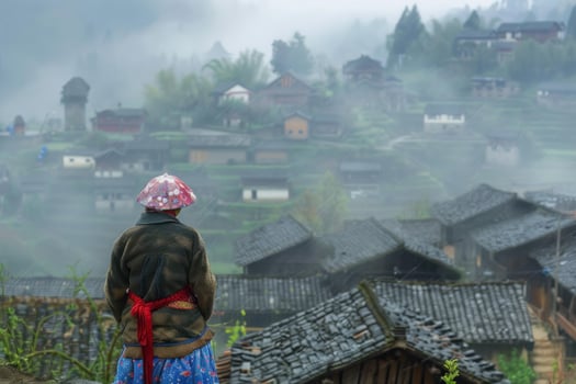 Local woman wearing traditional clothes and hat looking at remote village in the mountains photo
