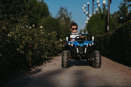 boy rides in toy mini car in park in summer photo