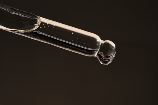 Pipette with serum on a dark beige background. photo