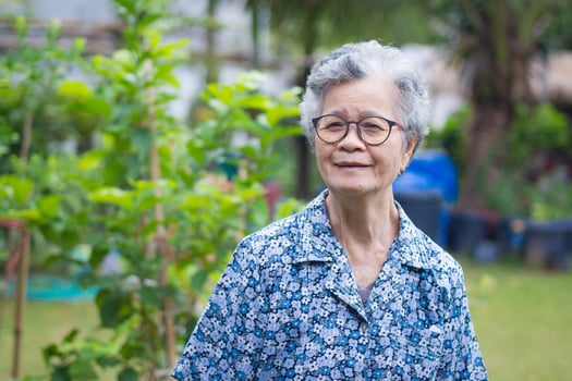 Senior woman wearing glasses with short gray hair smiling and looking at camera while standing in a garden. Space for text. Concept of aged people and healthcare photo