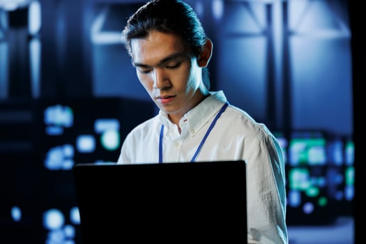 Dara center manager running code and programming on laptop, troubleshooting and upgrading high tech facility designed to accommodate rows of fully operational server supercomputers photo