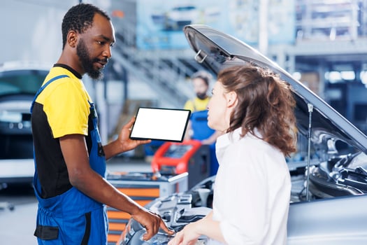 Mechanic in car service uses mockup tablet to order new engine for malfunctioning vehicle. Adept garage workspace expert shows woman needed parts replacement on isolated screen device photo