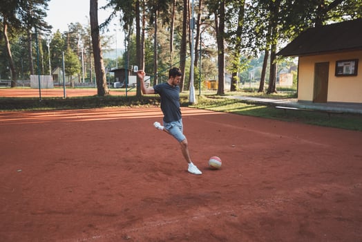 Black-haired athlete plays with a balloon on a clay court. Amateur sport. Individual football training. Soccer. Kicking, striking, passing and dribbling photo