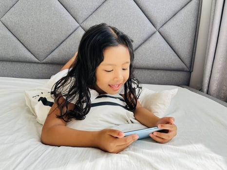 Little child girl watching cartoons on mobile phone. Asian kid watching smartphone laying on the bed at home. Little girl addicted mobile phone. Technology and internet concept photo