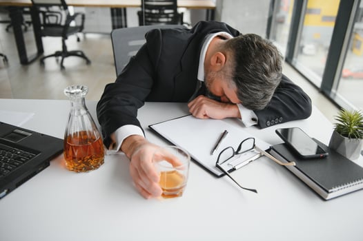 Close up of stressed businessman holding a glass of whiskey he sleeping and Data Charts,business document at office desk. alcohol addiction and drunk businessman concept photo