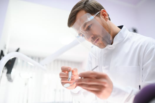 Bottom view young confident happy professional stomatologist european doctor man 20s in white gown hold showing tooth drilling machine at dentist office indoor cabinet. Healthcare aesthetic treatment. photo