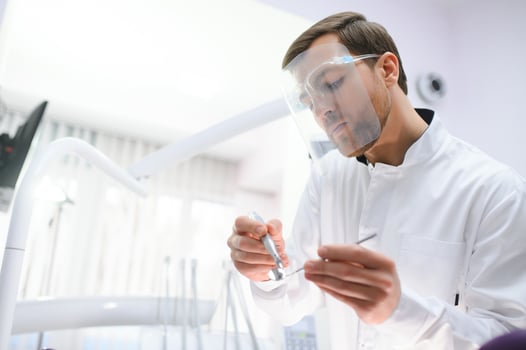 Bottom view young confident happy professional stomatologist european doctor man 20s in white gown hold showing tooth drilling machine at dentist office indoor cabinet. Healthcare aesthetic treatment. photo
