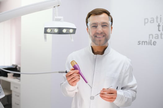 Attractive male dentist in doctors white lab coat posing in modern dental office photo