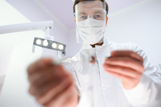 Bottom view young confident happy professional stomatologist european doctor man 20s in white gown hold showing tooth drilling machine at dentist office indoor cabinet. Healthcare aesthetic treatment. photo