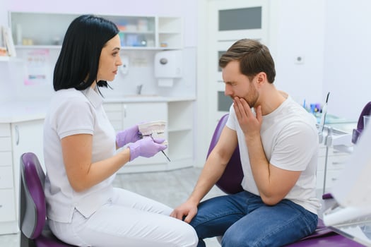 Sad man sitting in dental chair suffering from acute tooth pain, rubbing his cheek, close up. photo