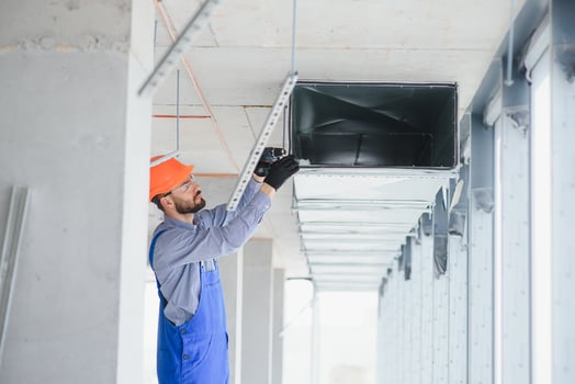 Industrial Theme. Warehouse Heating and Cooling System Installation by Professional Caucasian Technician. Commercial Building Ventilation Rectangle Canals. Air Distribution. photo